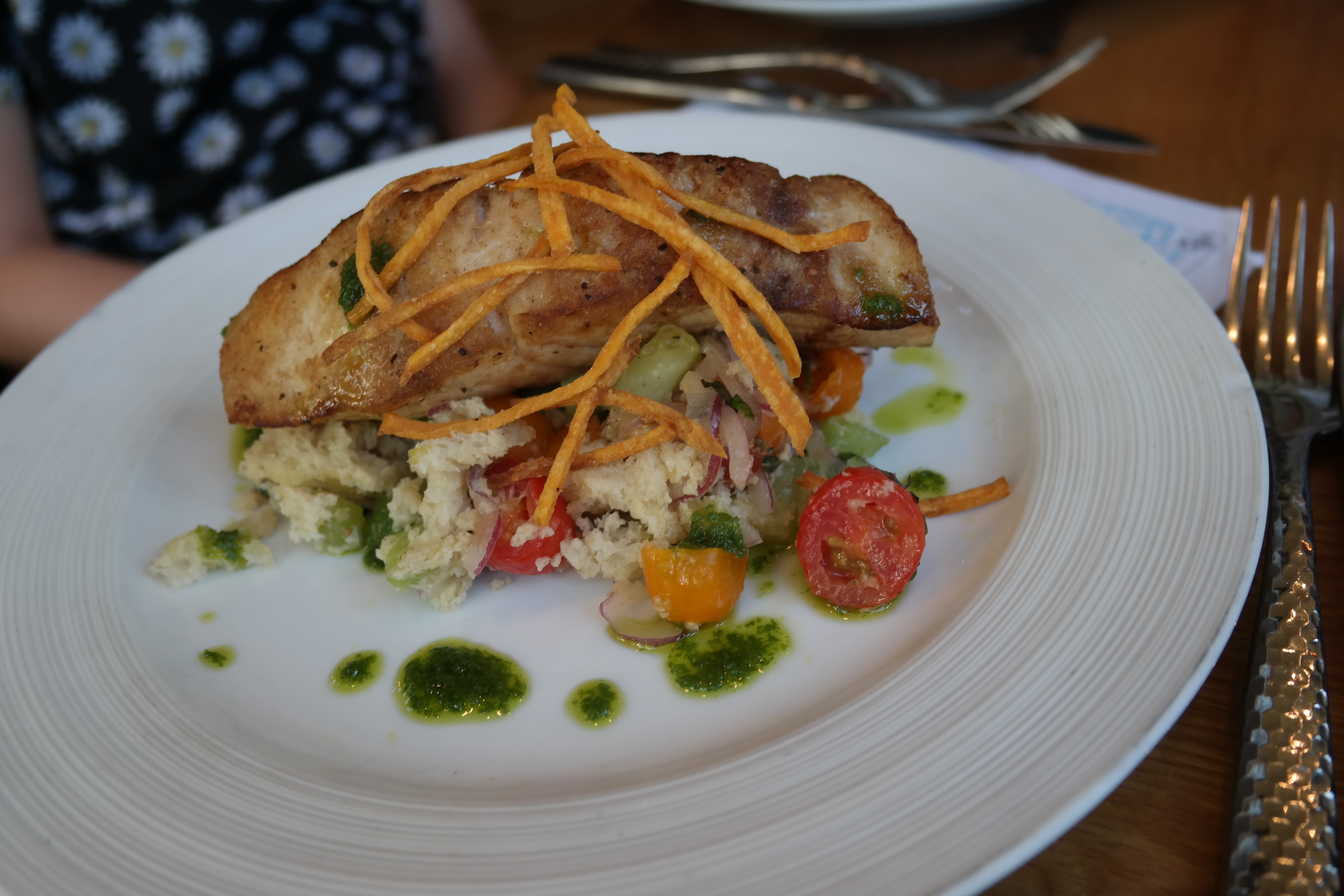 A perfectly cooked piece of fish with a sweet potato hay and delicious goodies underneath.