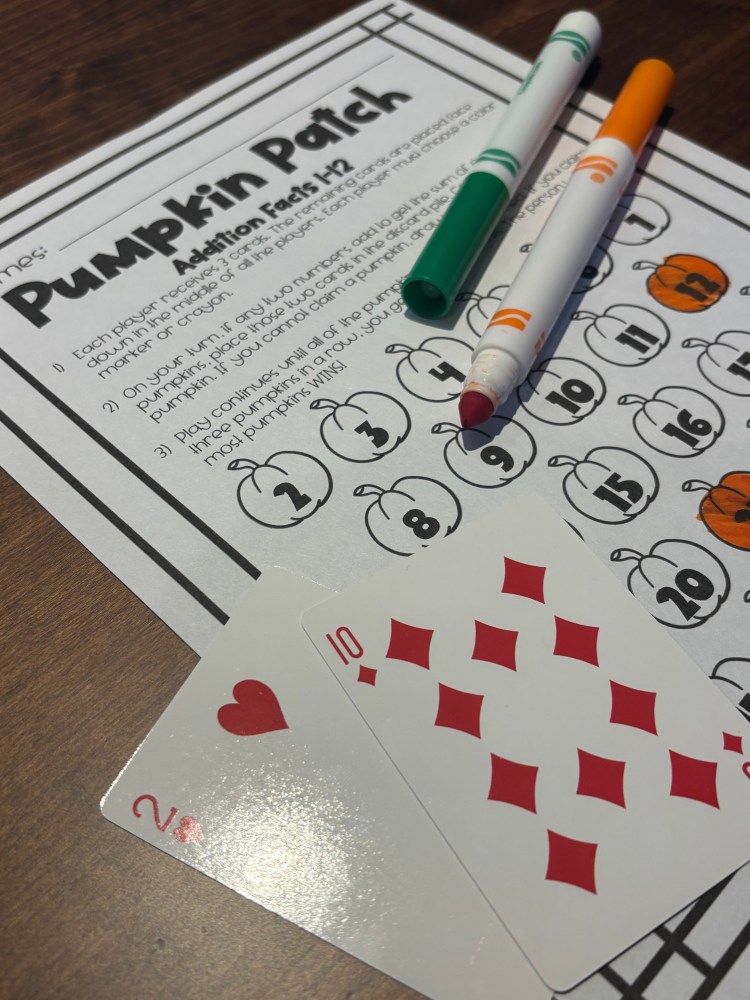 A Pumpkin Patch activity sheet featuring addition facts with pumpkins and numbers, accompanied by colored markers and playing cards showing the numbers 2 and 10.