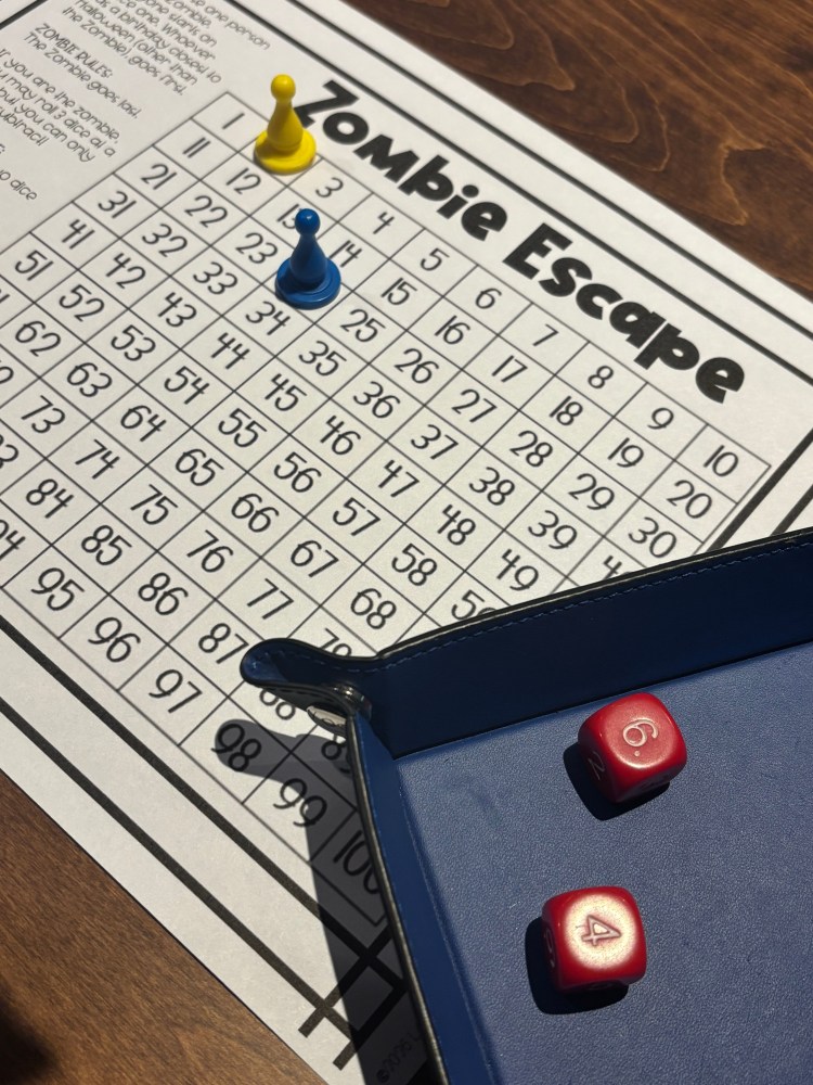 A top-down view of a tabletop game named 'Zombie Escape' featuring a game board with numbered squares, yellow and blue player pieces, and two red dice showing the numbers 6 and 4.