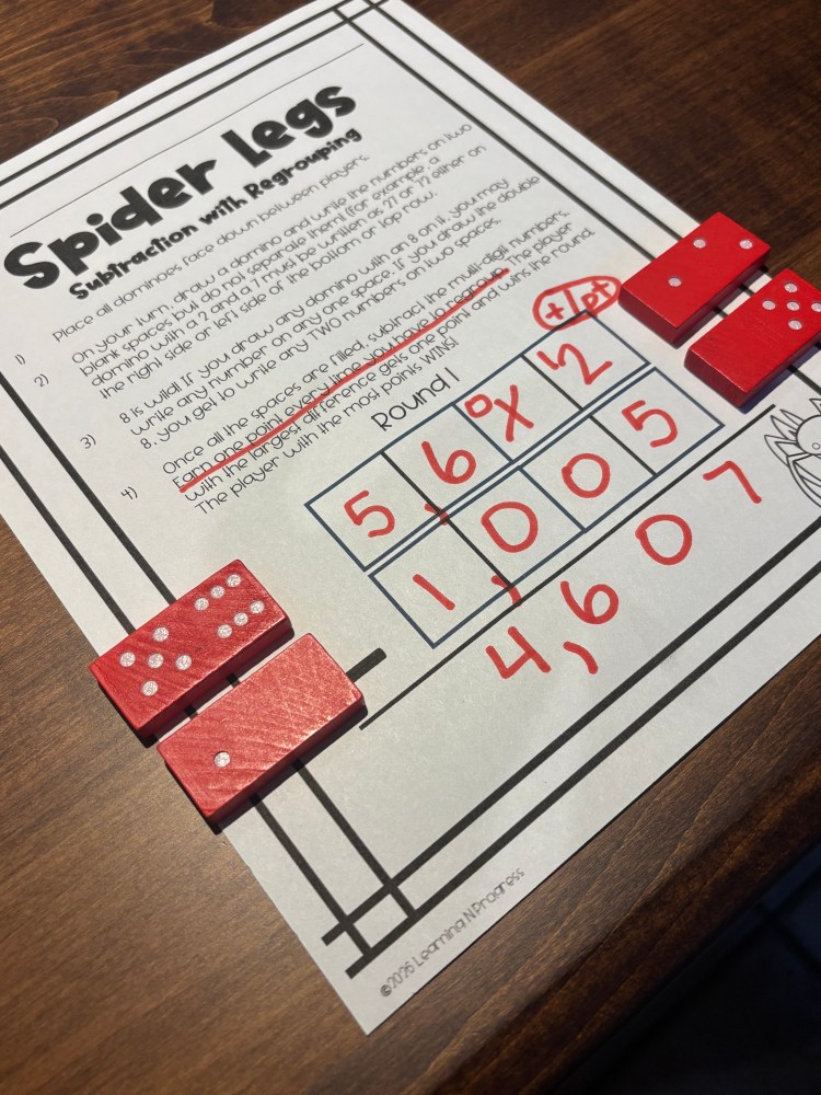 A printed game sheet titled 'Spider Legs' with instructions for subtraction with regrouping, accompanied by red dominoes showing various dots, and a score table filled with numbers.