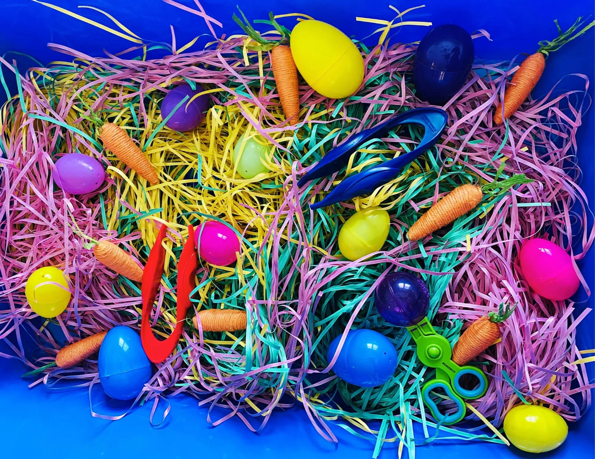 simple easter sensory bin with paper easter grass, yarn wrapped carrots, tongs and plastic eggs