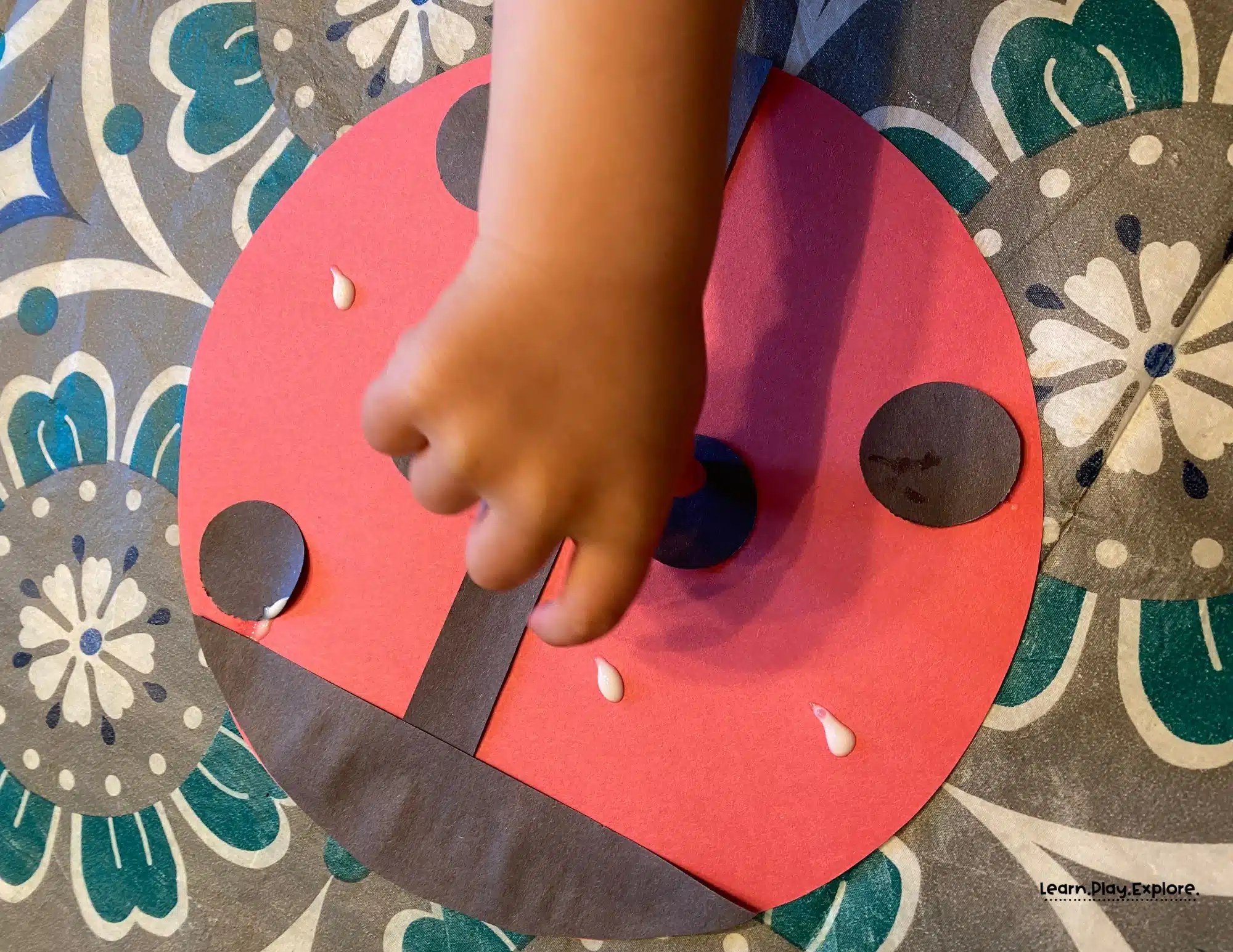 toddler gluing black paper circles onto red paper for ladybug craft