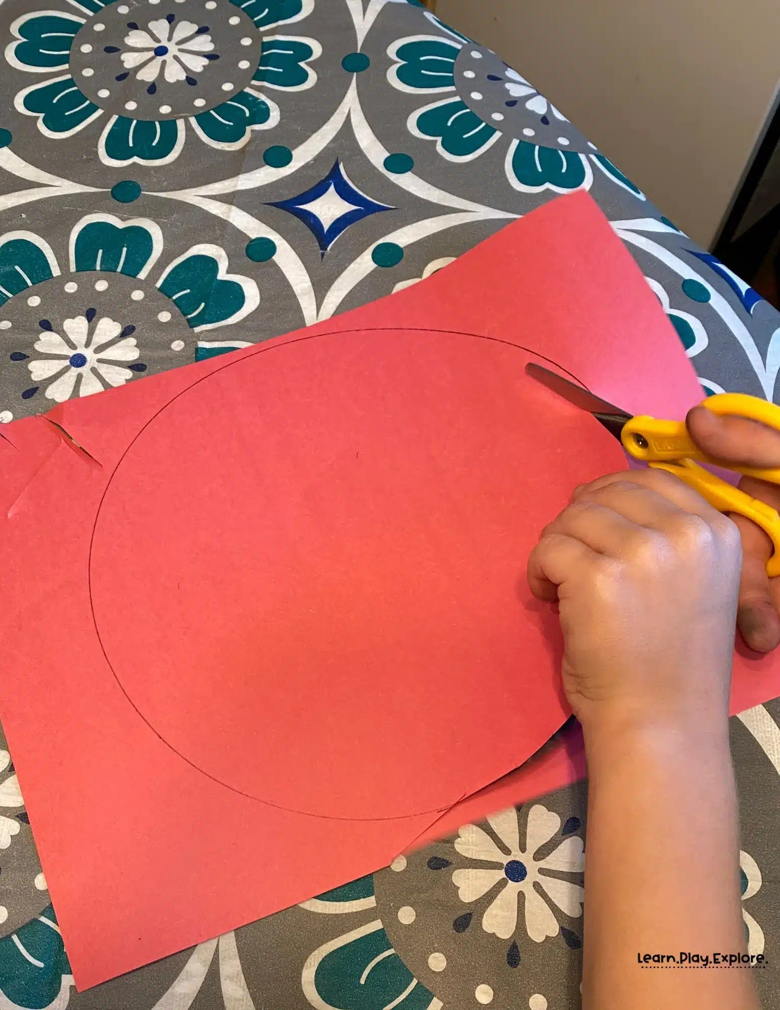 Child cutting out circle shape from red construction paper