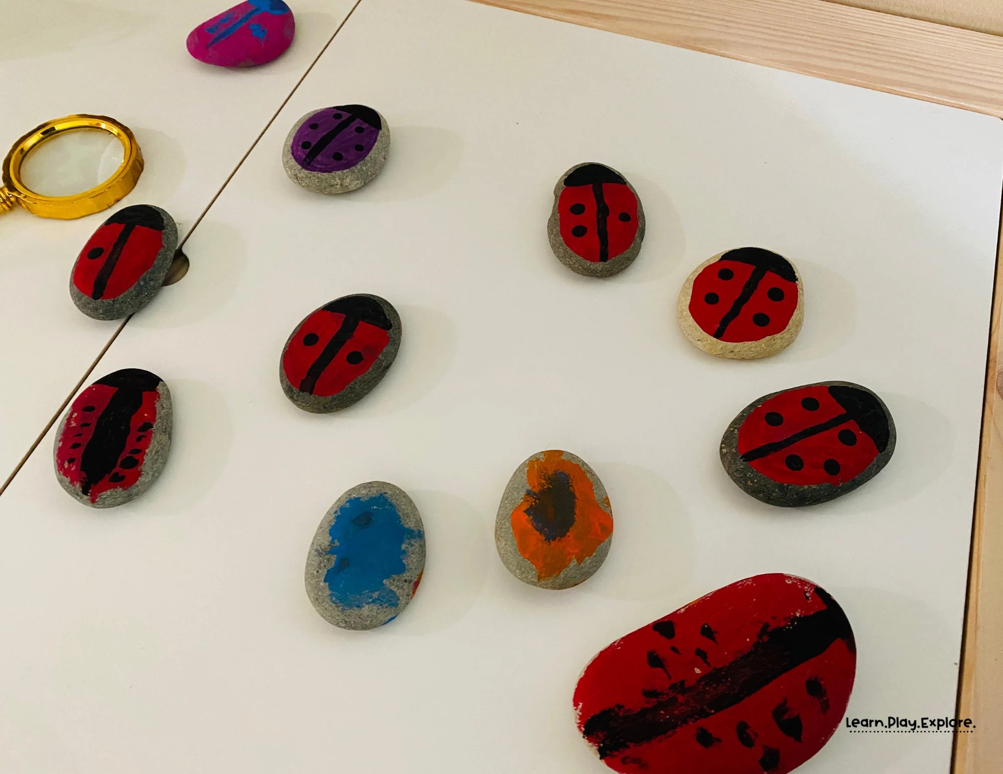lots of painted rocks sitting on a closed sensory table with a magnifying glass