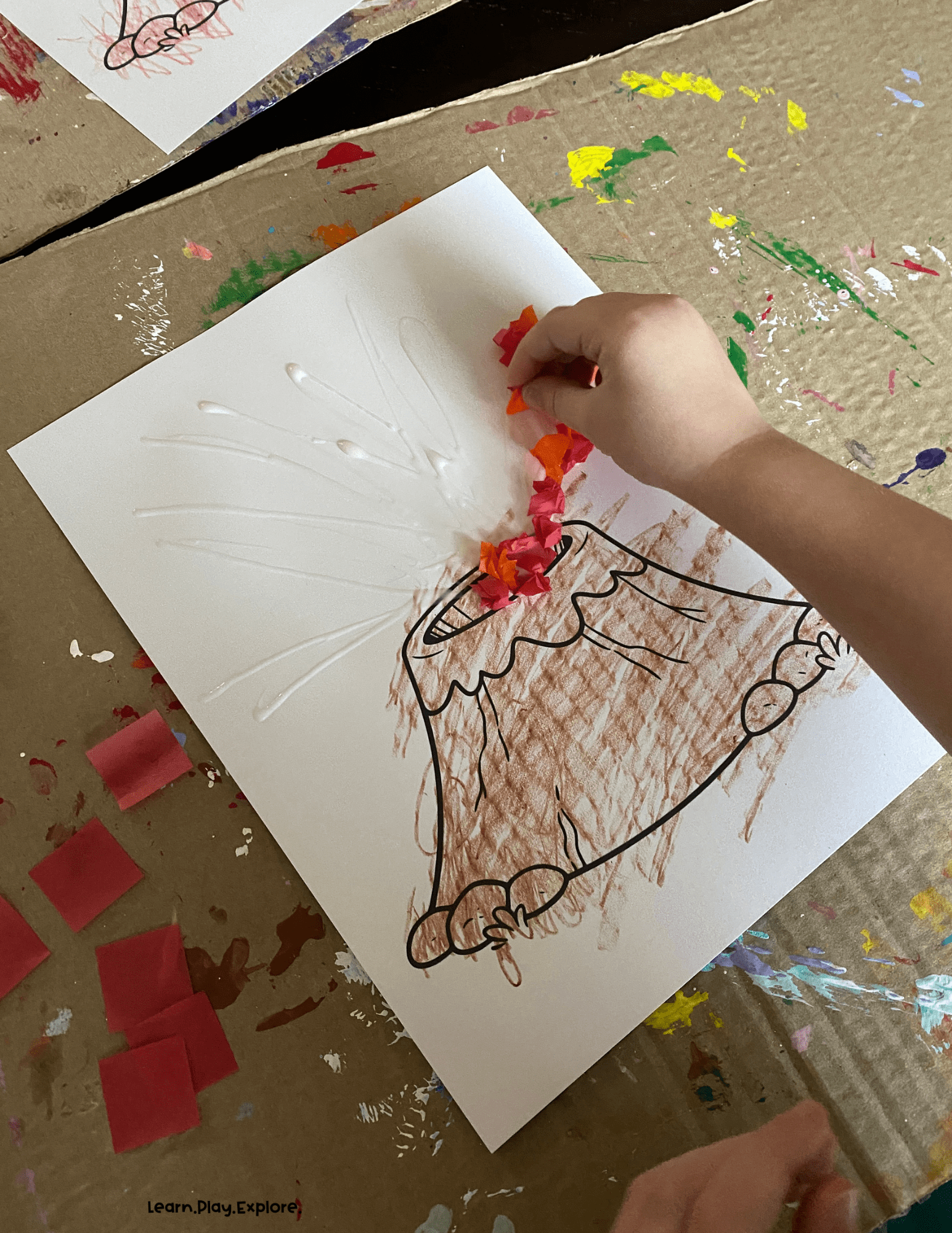 a toddler pinching tissue paper above a printed out volcano
