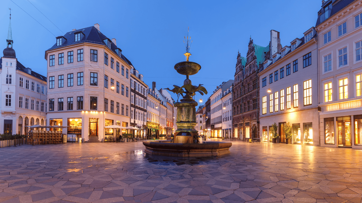 The illuminated Stork Fountain surrounded by historic buildings in Amagertorv square at dusk, one of the must-see places in Copenhagen’s shopping district.