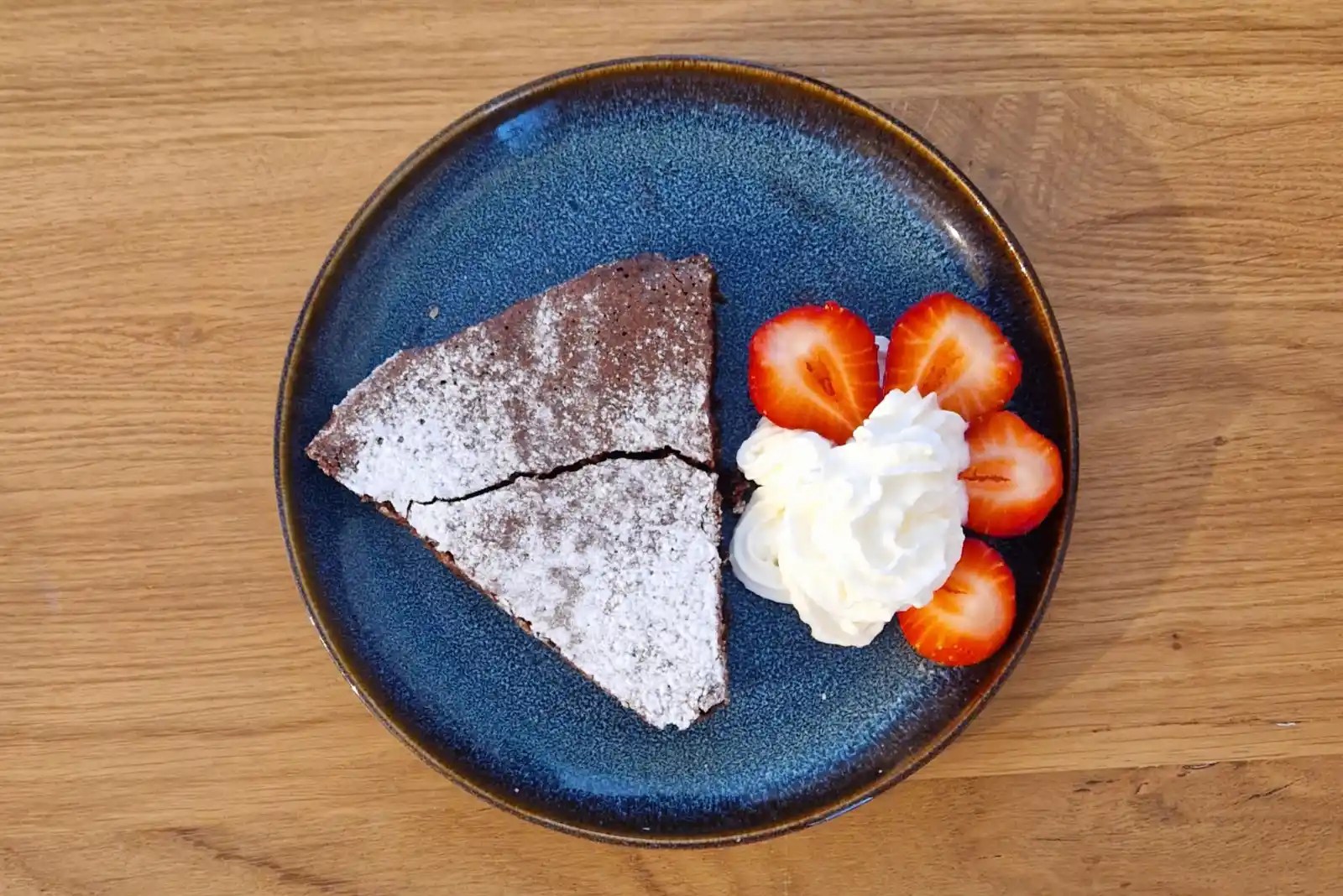 A slice of Swedish chocolate mud cake served with whipped cream and strawberries on a blue plate, made to celebrate kladdkakans dag.