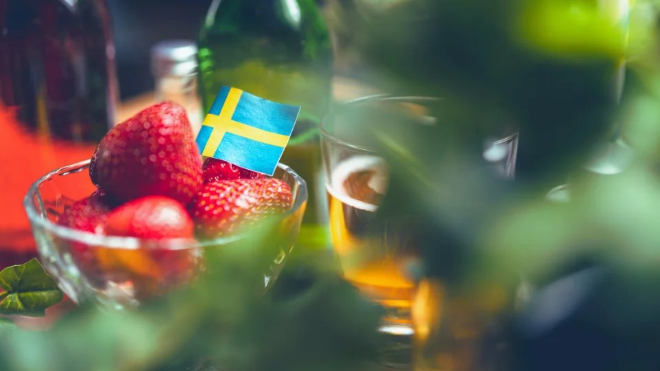 Fresh strawberries with a small Swedish flag and a glass of cider - a taste of Swedish culture, one of the best ways to learn Swedish.