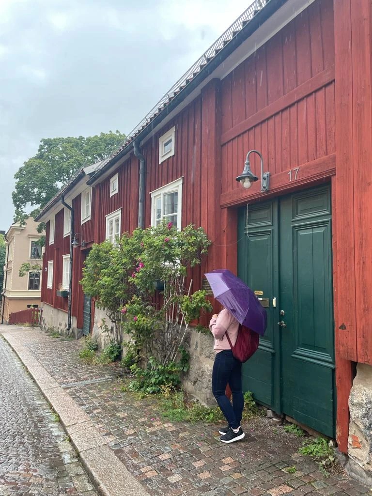 Yanitsa with a purple umbrella in front of red wooden houses in Uppsala.