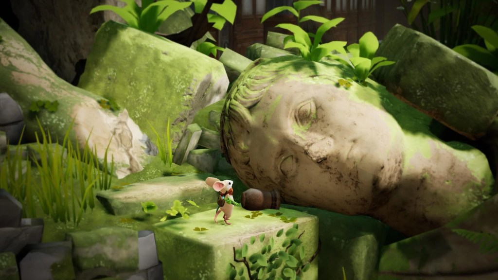 Une petite souris se tient devant une grande tête de statue en pierre recouverte de mousse, entourée de rochers et de plantes vertes.