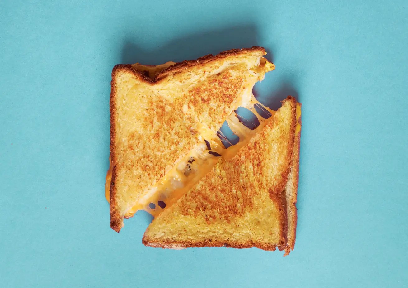Un « grilled cheese » (sandwich au fromage grillé) doré sur un fond bleu.