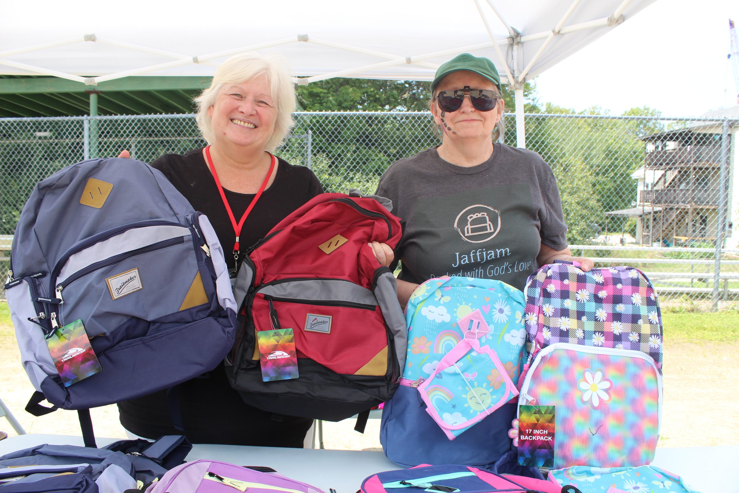 Volunteers Laura Thibault and Marie Straitiff hand out free backpacks to children at Jaffjam 2025.