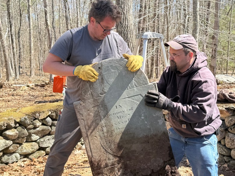 Ka Nalenz of Gravestone Services of New England and volunteer Walter Gruda lift the slate gravestone out of the cemetery.