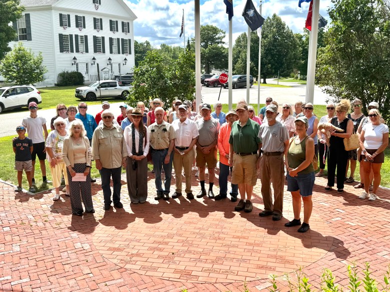 A group of veterans, at the front, with members of the public and the Rindge Woman's Club, in front of the brick memorial at Veterans Park in Rindge. 