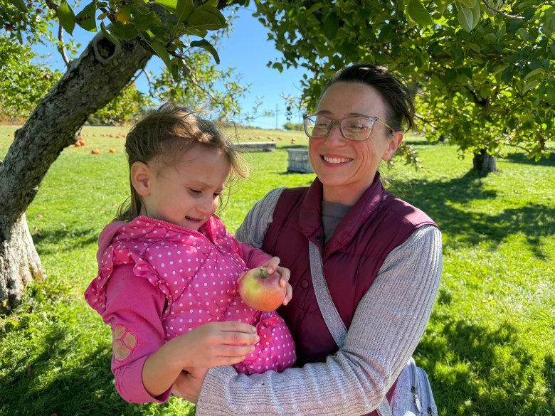 Felicity Caron, held by her mother Brina Caron of Ashby seeks out an apple among the branches of a tree at Washburn's Windy Hill Orchard in Greenville. 
