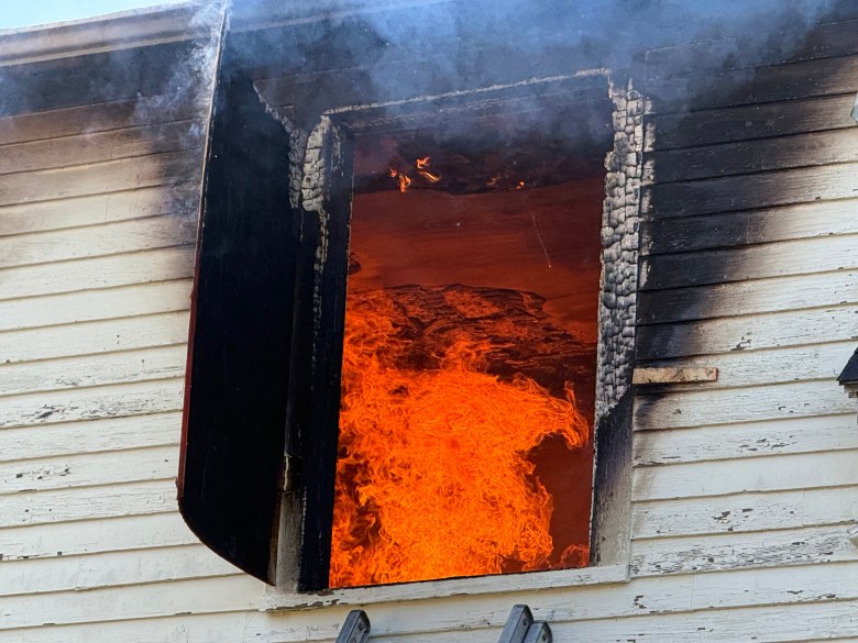 Flames in the second story of the house show through the window.