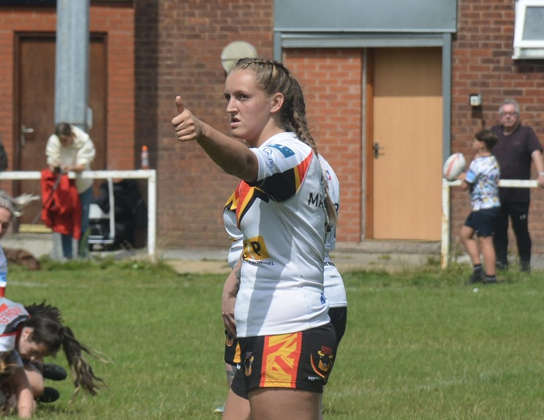 A girl in a white top and black shorts posing with her thumbs up.