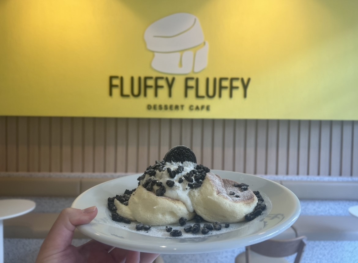 A hand holding a plate of oreo pancakes in front of the Fluffy Fluffy dessert cafe sign