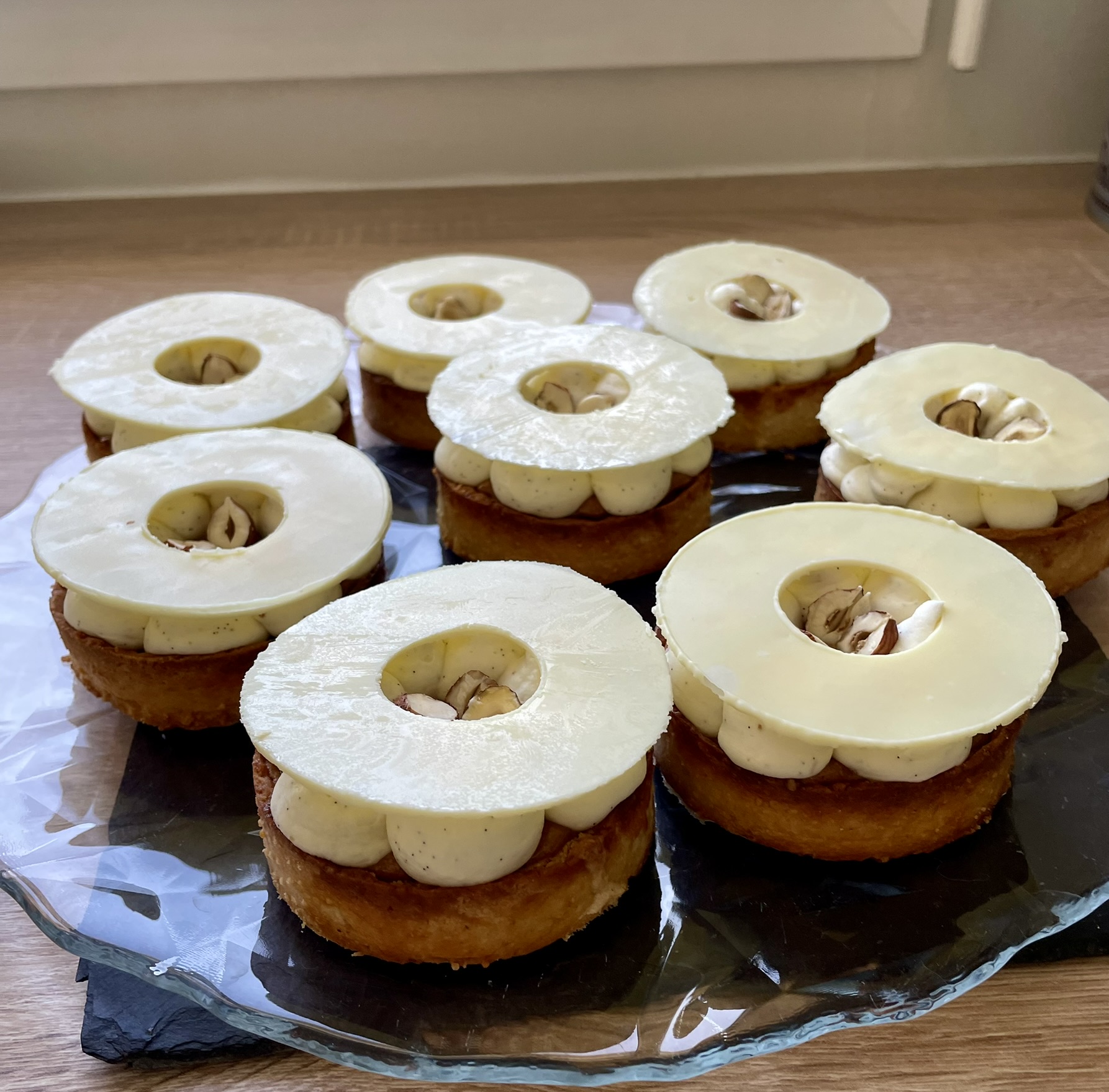 Tartelettes à la noisette et à la vanille, avec une ganache pochée, un cercle de chocolat blanc et des noisettes au centre