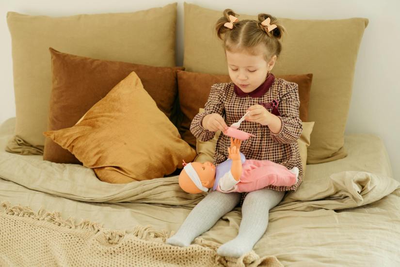 Girl in plaid dress playing with baby doll, following a speech teletherapy session