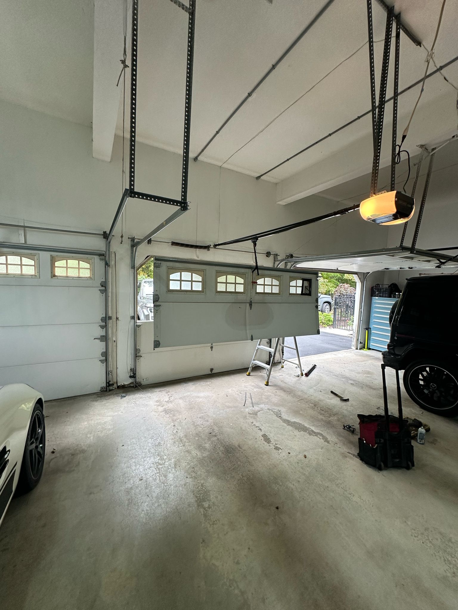 White garage door in front of harage doors with rails of garage door openers and a cement floor.