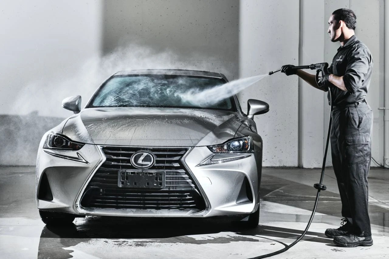 Lexus technician pressure washing exterior of silver Lexus vehicle