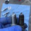 Comparison of new and worn spark plugs in technician’s hand