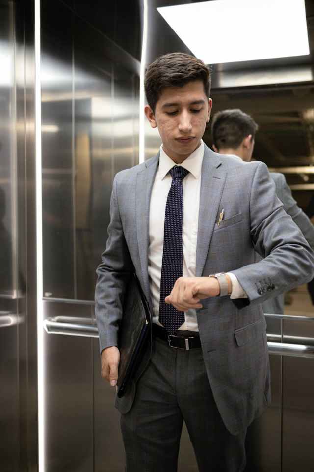 Businessman in a gray suit checking time in an elegant elevator setting.
