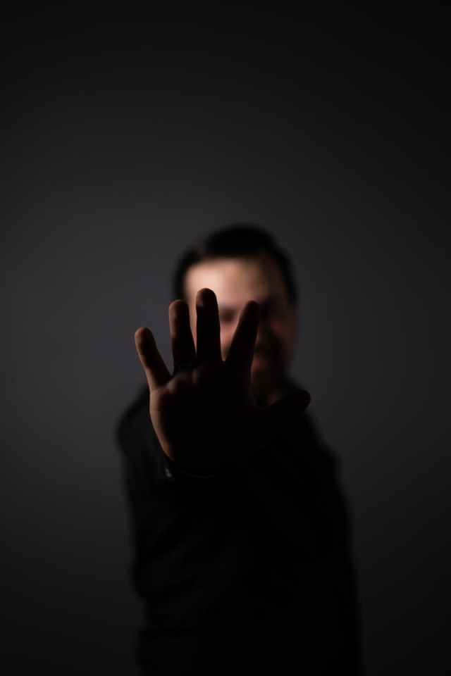 Blurred person holding out hand in dark studio with focus on gesture.
