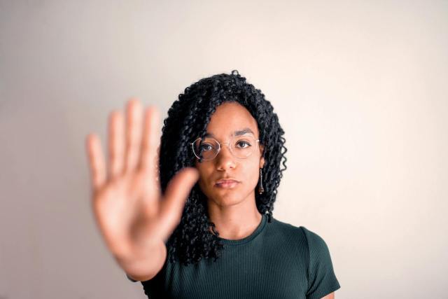 Young black woman with glasses shows stop gesture, expressing confidence and style.