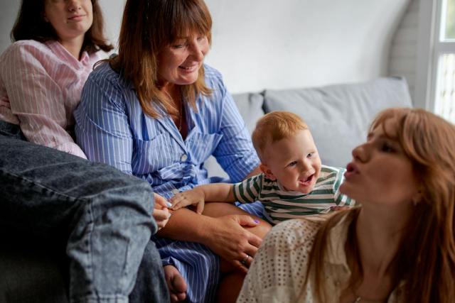 Crop content female relatives playing with cute cheerful baby on sofa in living room