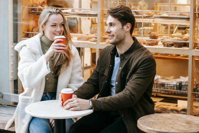 Young couple enjoying coffee outdoors near a bakery, capturing a moment of joy and connection.