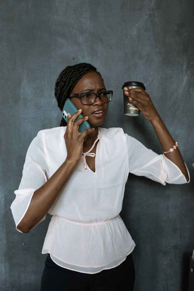 Businesswoman in a white blouse on a phone call, appearing frustrated while holding a coffee cup.