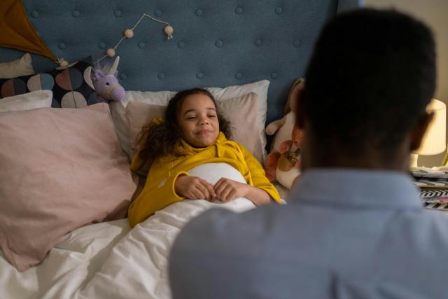 A father lovingly tucks his daughter into bed, creating a calm nighttime scene.