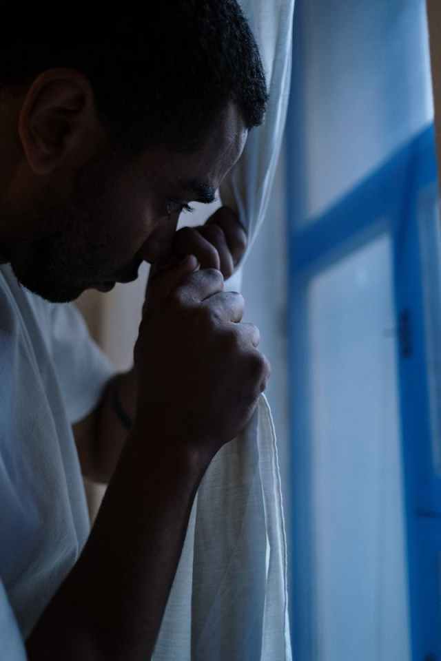 A man in deep thought peeping through curtains at home, depicting solitude and introspection.