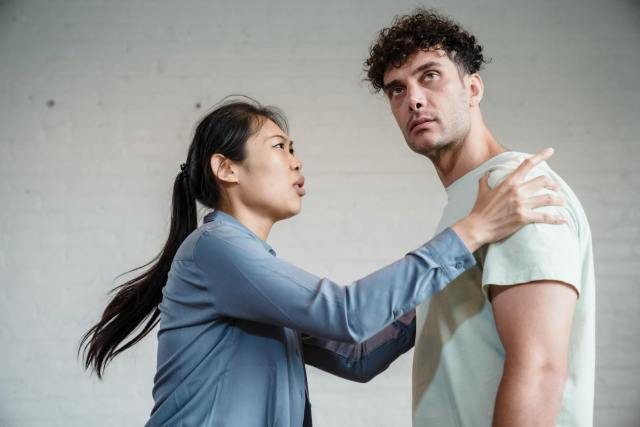 An Asian woman and Caucasian man engaged in an emotional discussion against a brick wall.