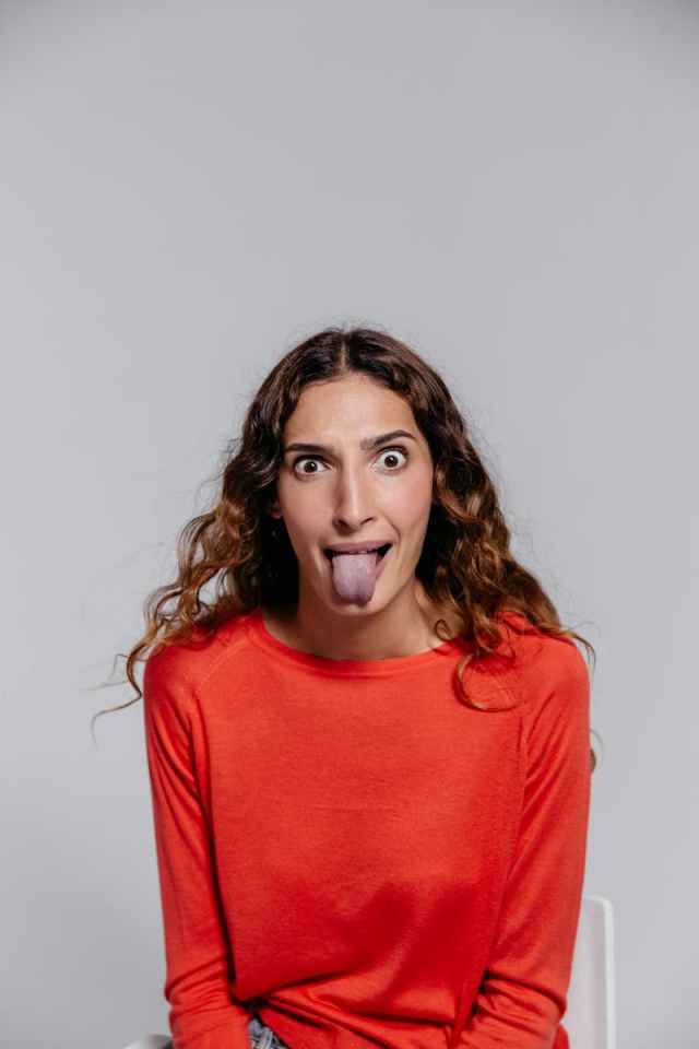 A woman in a red top makes a playful face, sticking her tongue out for a humorous portrait.