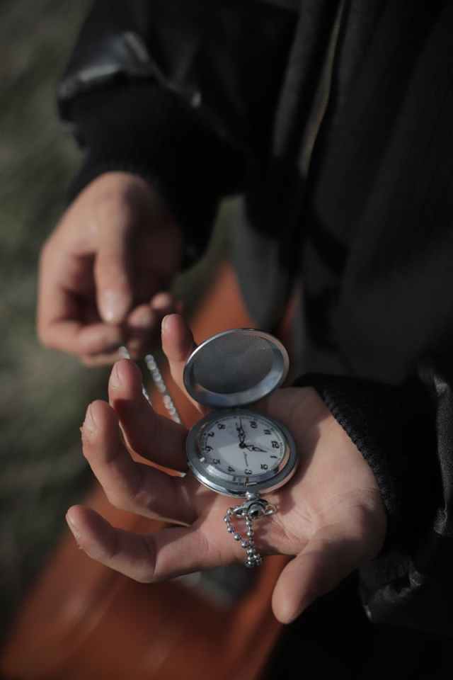 A close-up of hands gently holding an antique pocket watch against a blurred outdoor background.