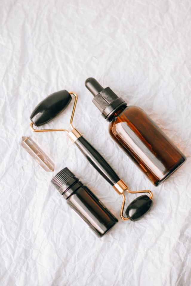 Flat lay of essential oil bottles and face roller on a textured white background.