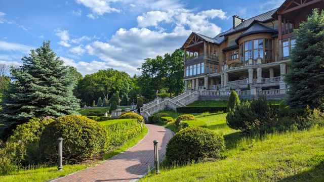 Stunning wooden manor surrounded by well-manicured gardens and vibrant trees under a clear blue sky.