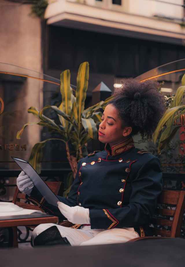 Stylish woman in vintage uniform exploring menu at outdoor cafe scene.
