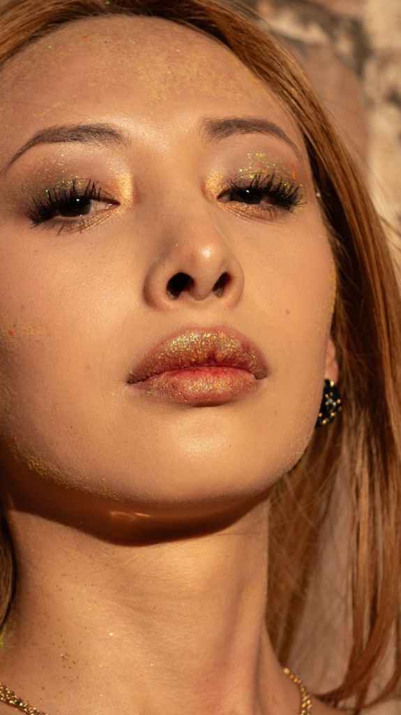 Elegant portrait of a woman with glittery makeup under warm sunlight, showcasing beauty and glamour.