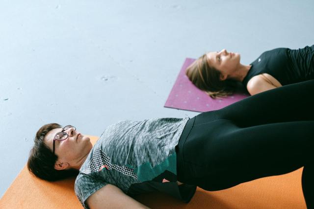 Two women performing floor exercises on yoga mats indoors in a fitness studio.