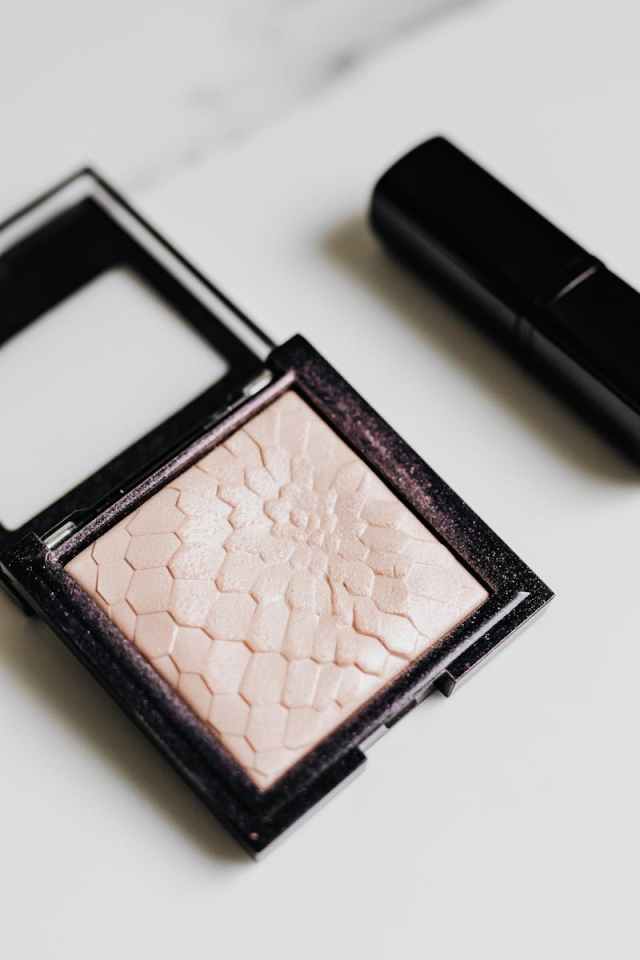 Flat lay of a textured highlighter compact and lipstick on a white surface, perfect for beauty and cosmetic themes.