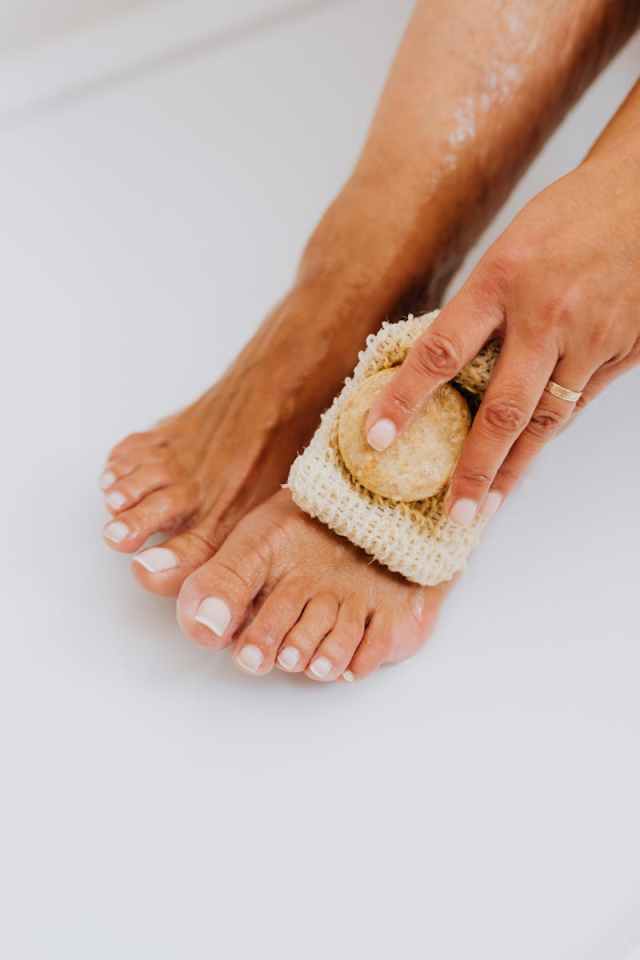 A close-up photo showing foot care using a loofah for exfoliation and maintenance.