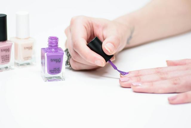 A close-up of a person applying purple nail polish as part of a manicure.