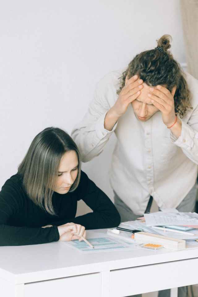 Young couple in discussion over financial papers, looking stressed at a table indoors.