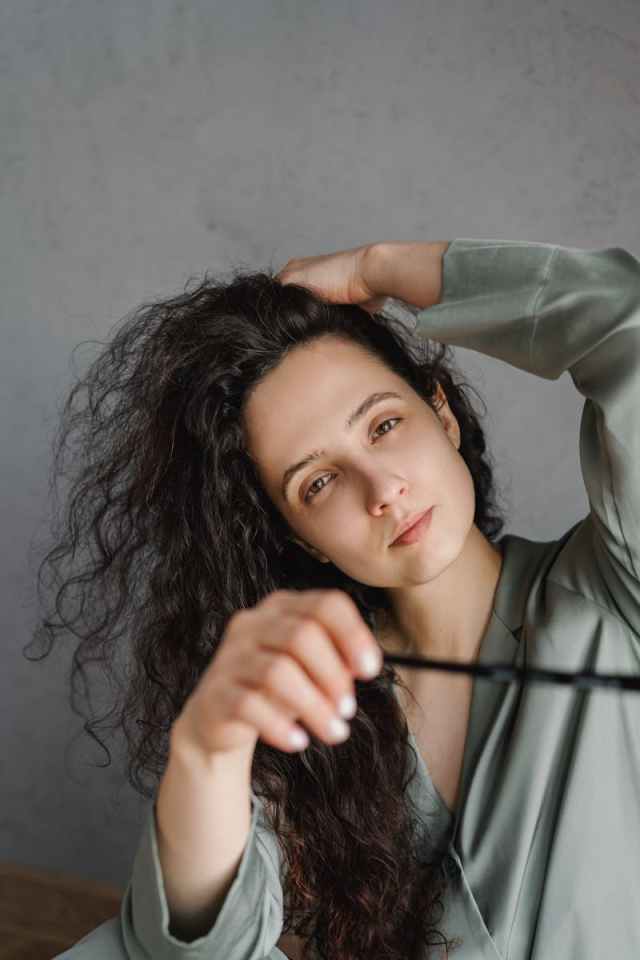 Close-up of a woman with messy hair, indoors wearing sleepwear, looking at the camera.