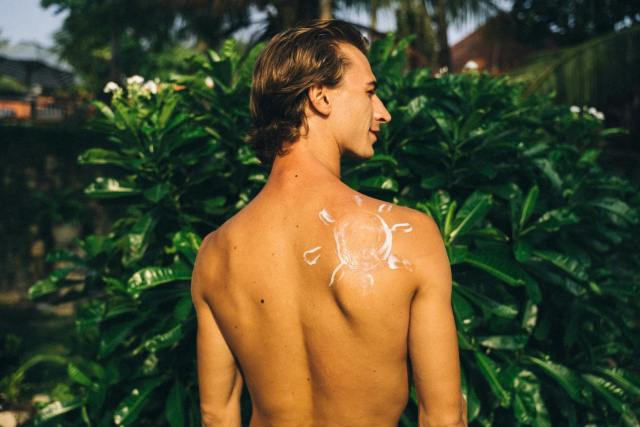 Back view of a shirtless man outdoors with a sun pattern on his shoulder.