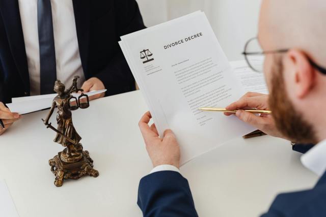 Two professionals examining a divorce decree with a Lady Justice statue nearby.